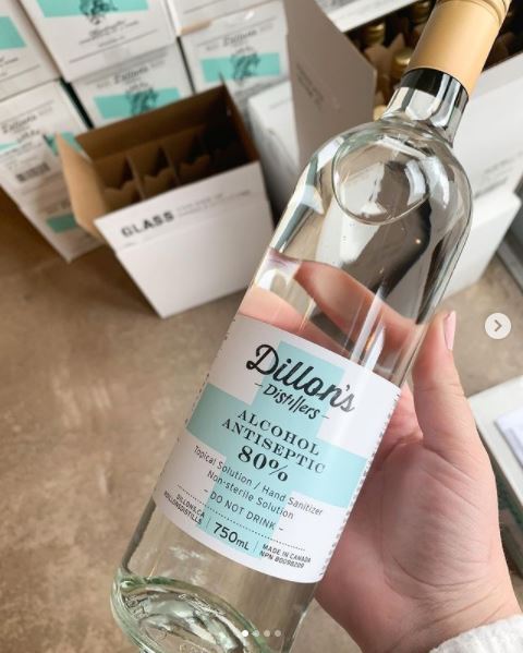 This is a picture taken of a person holding a bottle of hand sanitizer which is labeled: "Dillon's Distillers, Alcohol Antiseptic 80%."