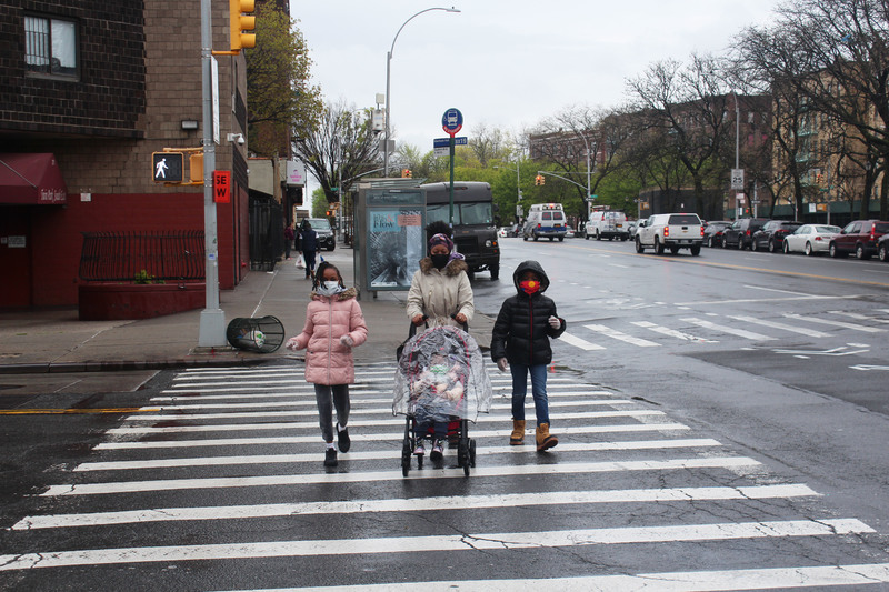 A family with masks on walking on a cross walk.