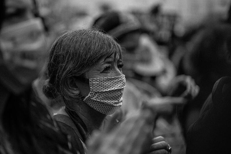 This is a black and white picture taken of an older Asian woman wearing a face mask in a crowd. 