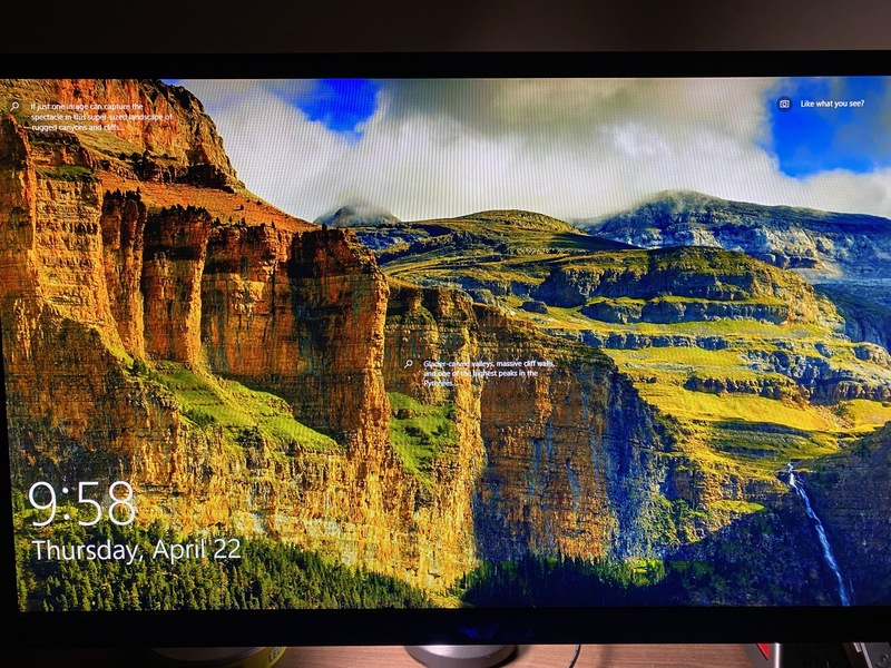 This is a picture taken of a desktop monitor, which has a mountain landscape as its screensaver. 