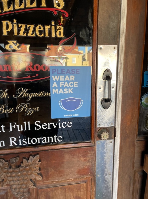 This is a picture of a sign posted on a pizzeria reading "Please wear a mask. Thank you". 