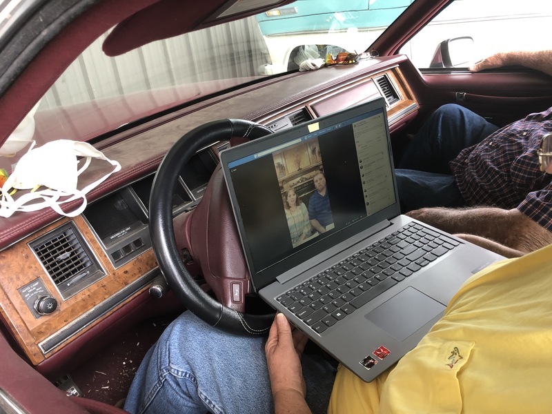 A photo of two people in a car, using a computer for a Zoom meeting.