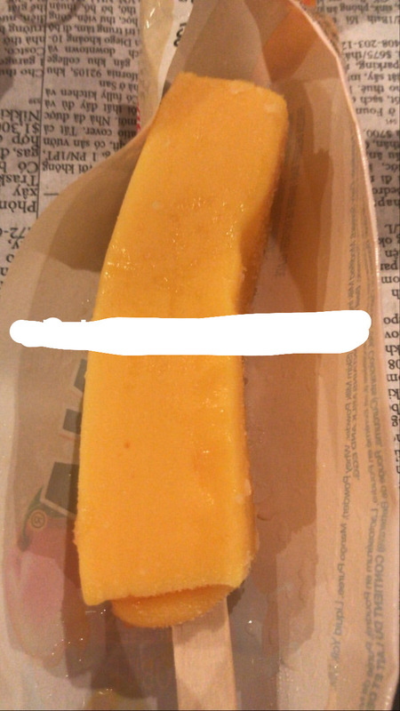 This is a picture taken of an orange ice cream pop in a wrapper. 