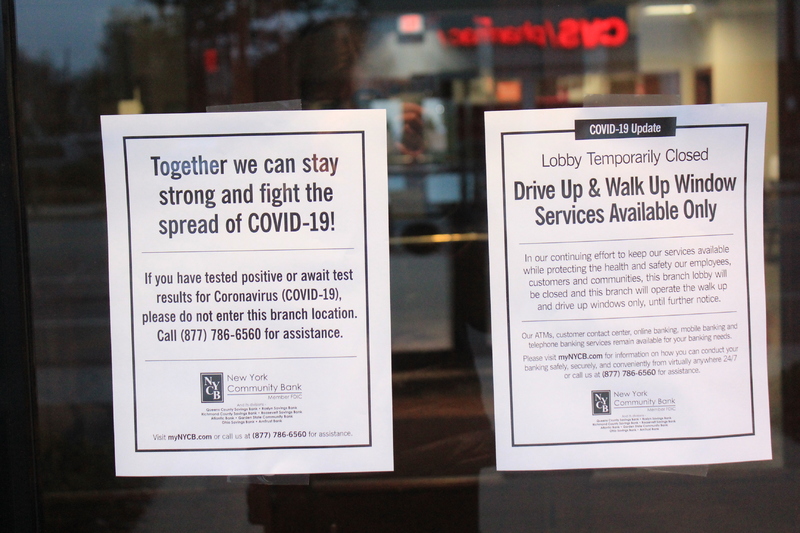 Two window signs from New York Community Bank. The first sign says "Together we can stay strong and fight the spread of COVID-19. If you have tested positive or await test results for Coronavirus (COVID-19) please do not enter the branch location. Call (877) 786-6560 for assistance."
The second sign says "COVID-19 Update. Lobby temporarily closed. Drive up & walk up window services available only. In our continuing effort to keep our services available while protecting the health and safety of our employees, customers, and communities, this branch lobby will be closed and this branch will operate the walk up and drive up windows only, until further notice. Our ATMs, customer contact center, online banking, mobile banking, and telephone banking services remain available for your banking needs. Please visit myNYCB.com for information on how you can conduct your banking safely, securely, and conveniently from virtually anywhere 24/7 or call us at (877) 786-6560 for assistance."