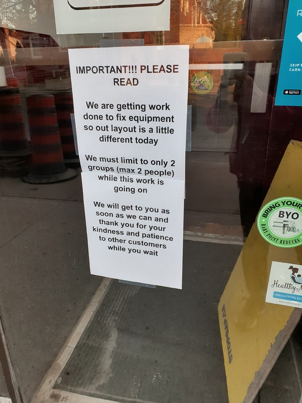 This is a picture of a sign in a businesses window which reads "Important!!! Please Read: We are getting work done to fix equipment so out layout is a little different today. We must limit to only 2 groups (max 2 people) while this work is going on. We will get to you as soon as we can and thank you for your kindness and patience to other customers while you wait."