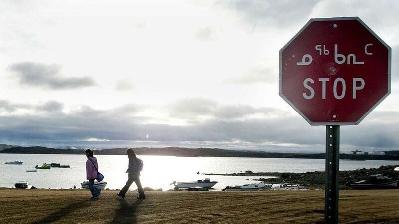 This is a picture of a stop sign with a body of water in the background. Another native language is written before the English word "STOP". 
