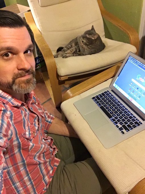 Image of a man taking a selfie with his cat while working from home.