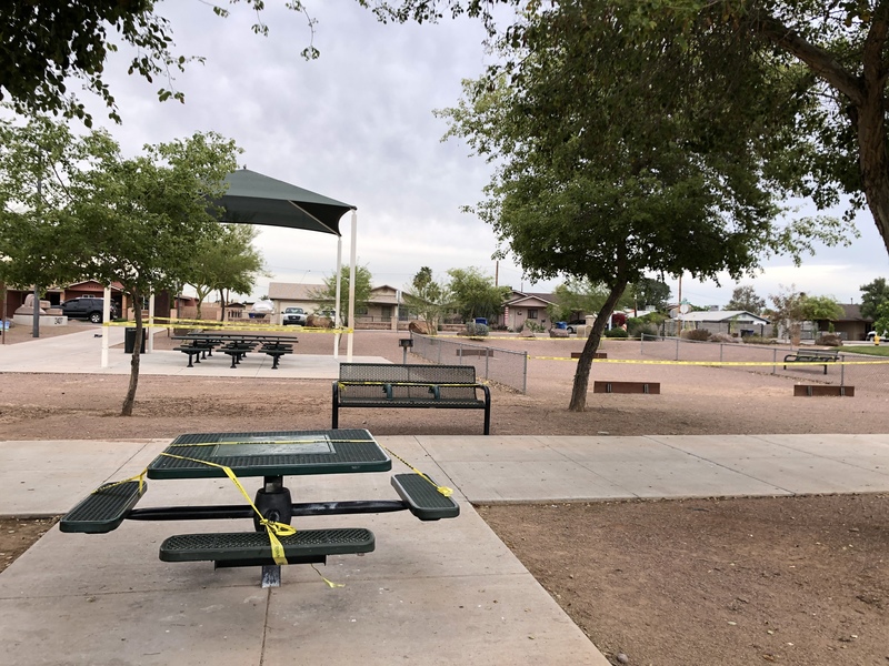 An empty park that has tables and chairs closed off with yellow caution tape. 