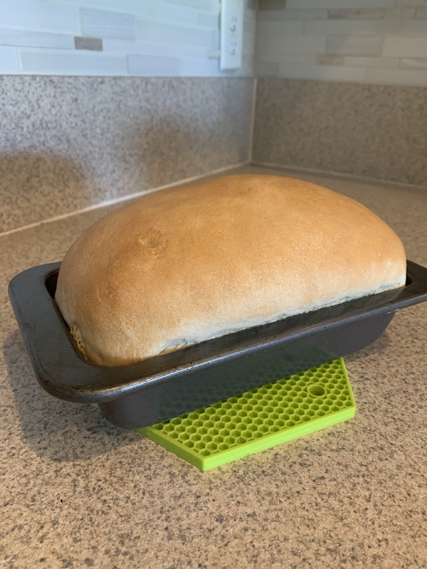 This is a picture of a loaf of freshly baked bread resting on a countertop in a kitchen. 