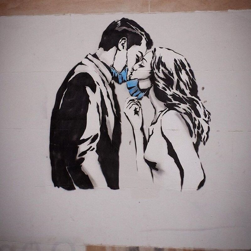 A mural on a wall depicting a man and a women kissing with masks pulled down over their chins. 