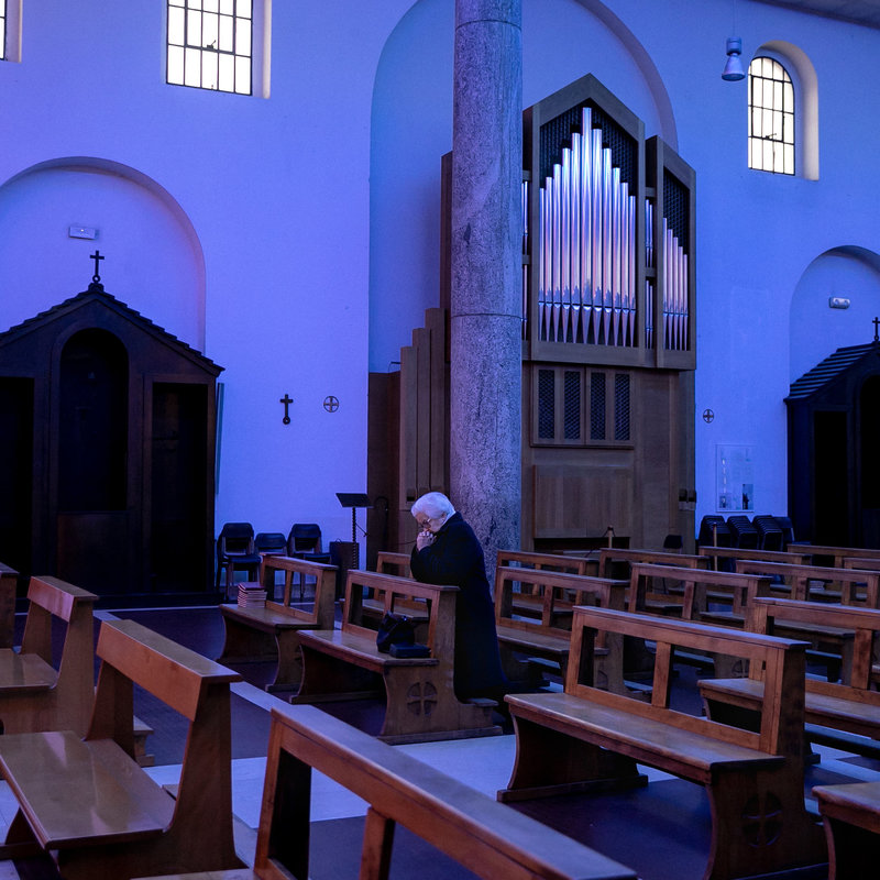 Inside of a church, a person is on their knees praying. 