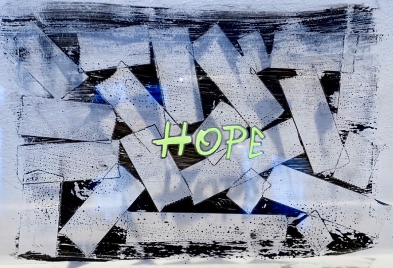 This is a picture taken of an abstract painting, made with dark grey colors and a message in the center that reads "hope". 