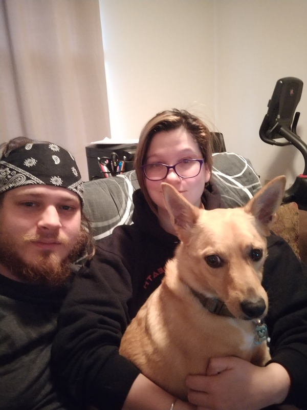 Two people are sitting on a couch with a dog in their lap. 