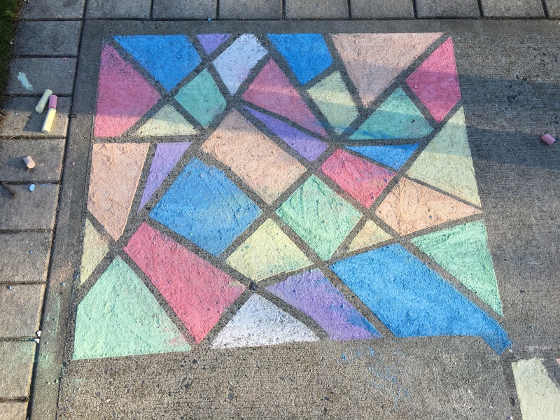 Sidewalk colored with chalk in multi-colors with geometric designs in a square.