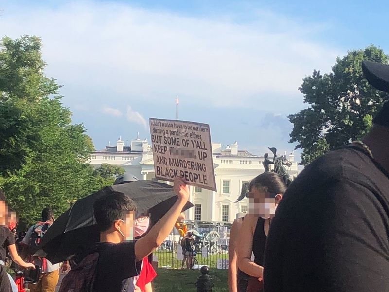 A person, whose face is blurred for privacy, attends a BLM protest holding a sign that reads "I didn't wanna have to be out here during a pandemic either, BUT SOME OF Y'ALL KEEP [blurred word]  UP AND MURDERING BLACK PEOPLE." 