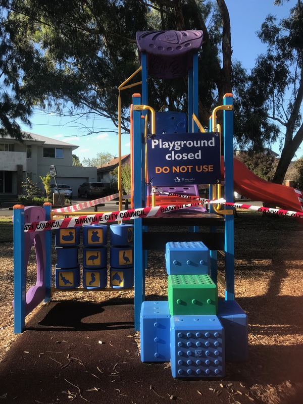 A playground that is taped off and has signs that say that the Playground is closed. 