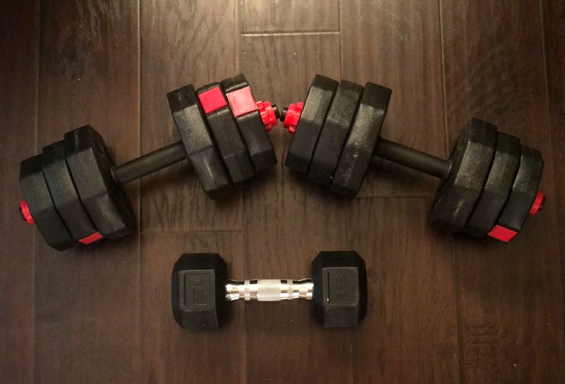 This is a picture taken of three dumbbells sitting on a wood floor.  