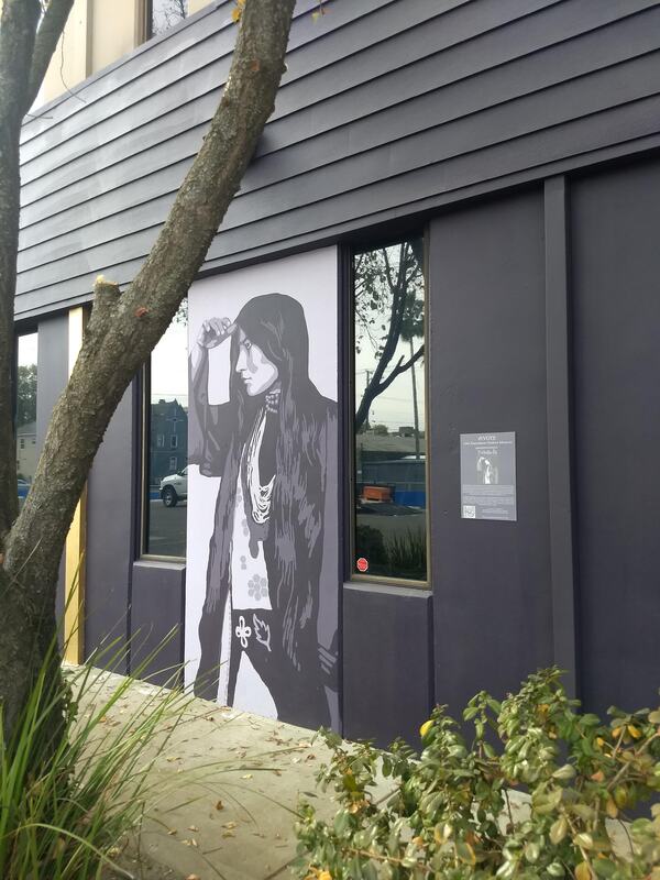 This is a picture taken of a mural that is painted on the side of a building. A woman is depicted in black and white. 