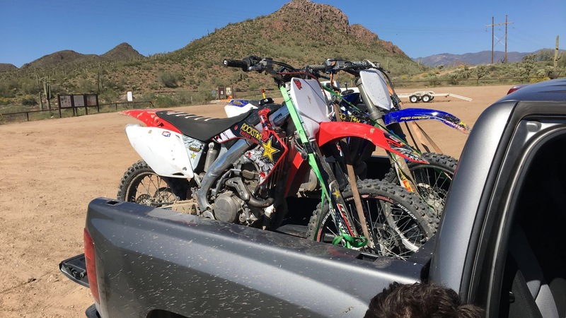 Two dirt bikes are on the back of a pickup truck. 