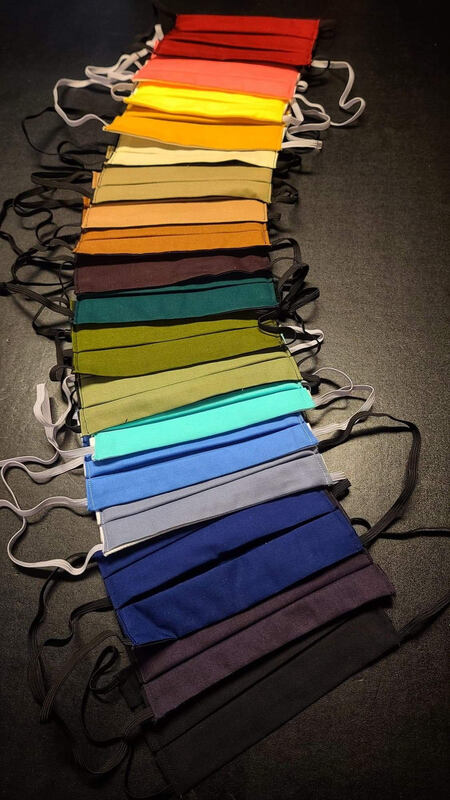 This is a picture of a collection of face masks that represent a rainbow of colors, laid out on a table. 