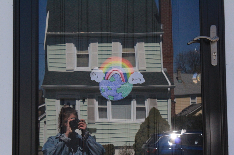 Residential house with a rainbow in the front door with the words "stay strong" on both ends and the world behind it. 