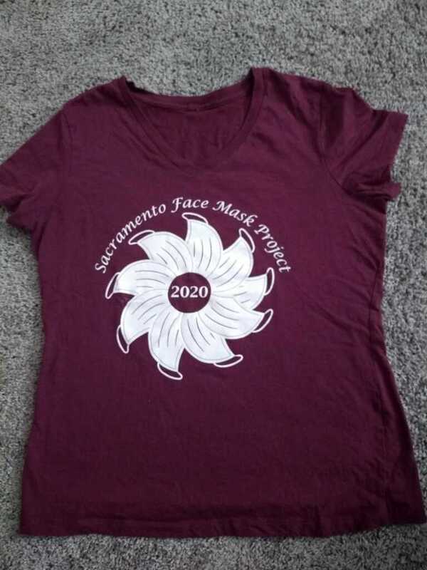 This is a picture of a red shirt which reads "Sacramento Face Mask Project". A wheel of face masks below these words are arranged to resemble a flower, with "2020" in the center. 