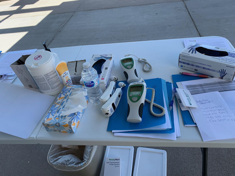 This picture shows a collapsible table with alcohol wipes, hand sanitizer, thermometers, and disposable gloves on it.  