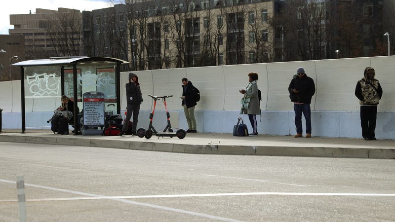 Numerous people waiting at a bus stop while practicing social distancing. 