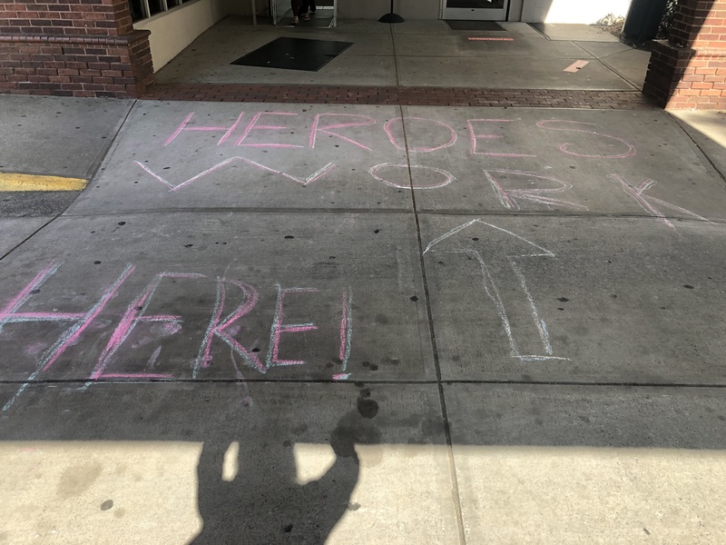 Chalk writing on sidewalk with an arrow drawn towards the doors and text, "HEROES WORK HERE!"