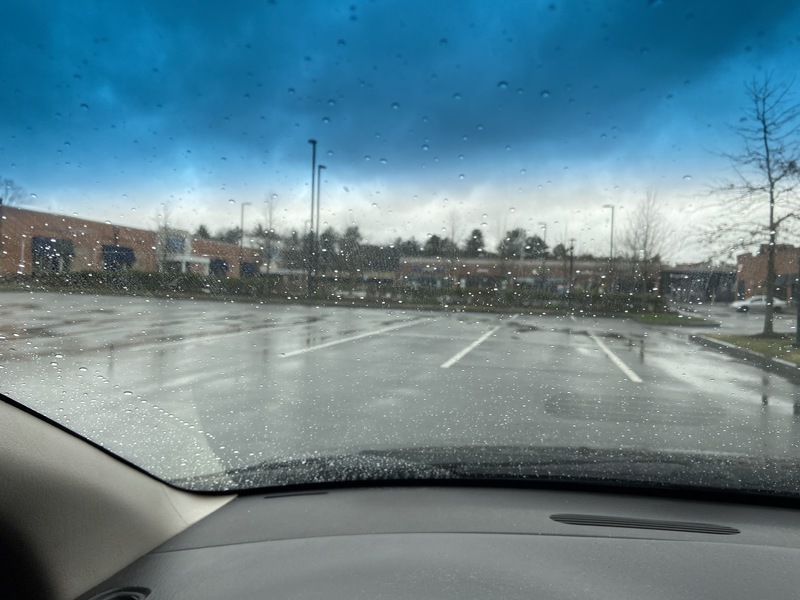 View out rained on vehicle windshield into an empty parking lot. 