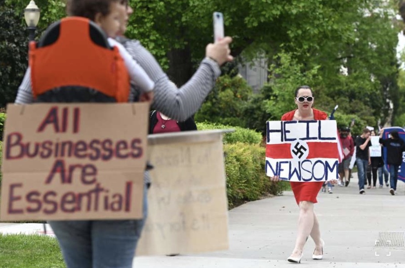 a person holding a sign that says "hail nihilism" and another person holding a sign that says "all jobs are essential" 