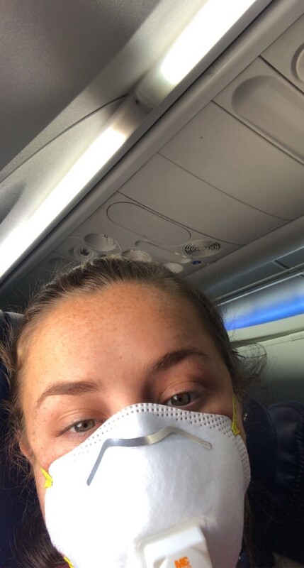 This is a picture taken of a woman sitting in a plane wearing a face mask. 