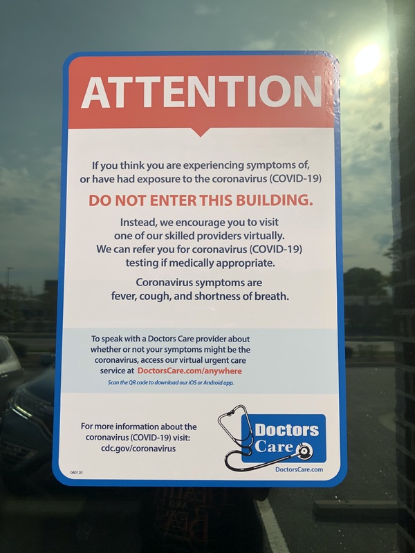 An attention sign at a doctor's office informing patients to use the virtual urgent care system instead of entering the building if patients have symptoms of COVID-19. 