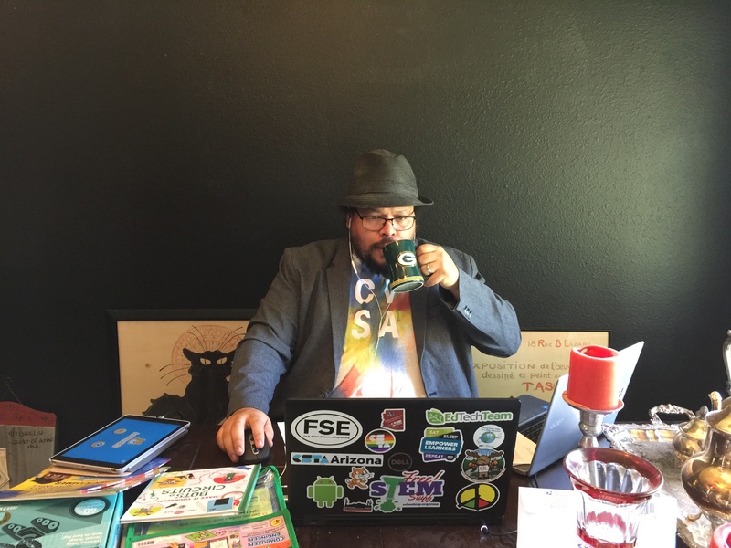 A person drinking out of a mug surrounded by school supplies looking at a laptop.