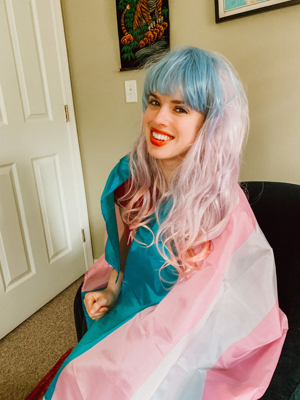 a woman wrapped in a trans pride flag and dyed pink and blue hair