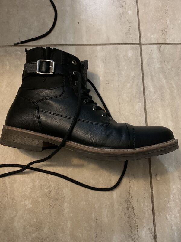 This is a picture of a leather shoe with laces and a buckle resting lengthwise on a tile floor. 