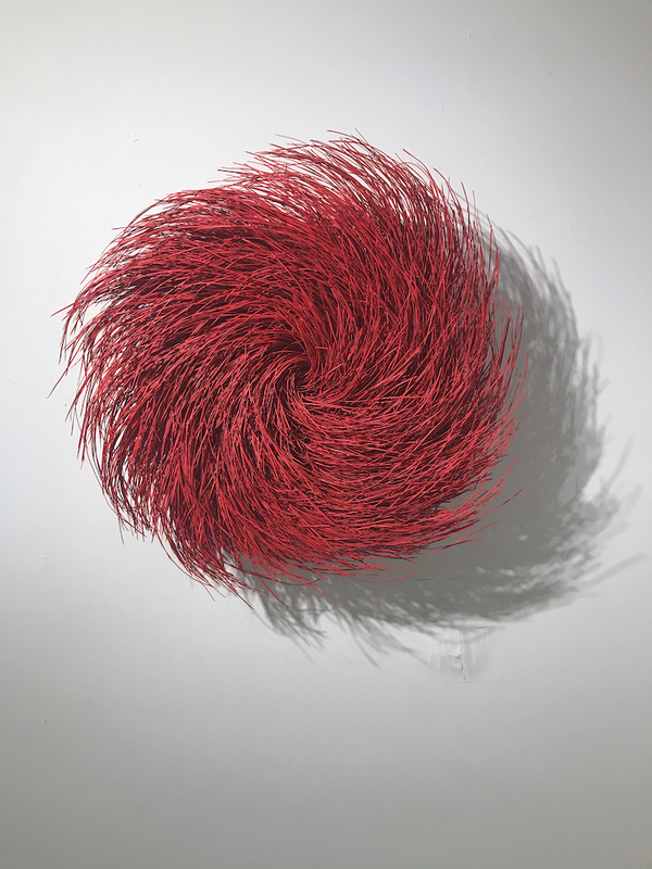 This is a picture of a mass of bight red, fluffy, stringy material which resembles a tassel or pom pom that is hanging on a wall.