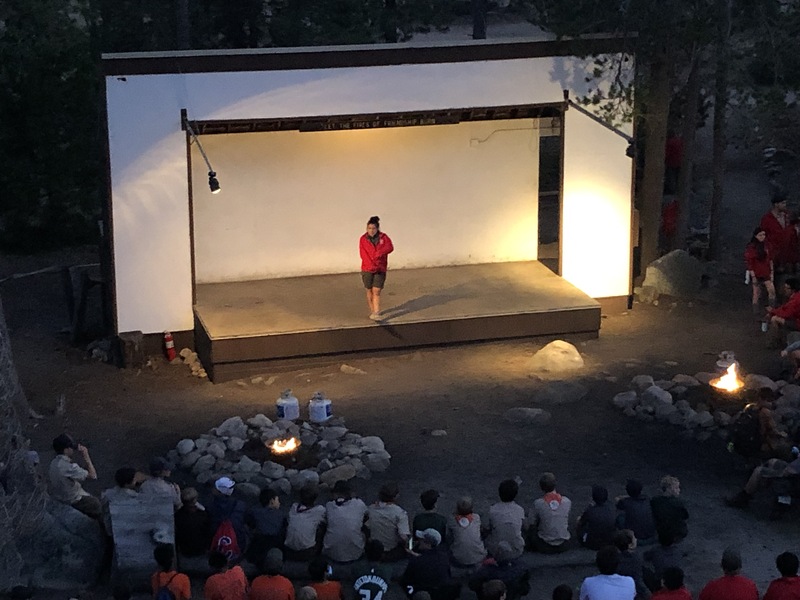 This is a picture of a person on a stage performing for an audience outdoors. 
