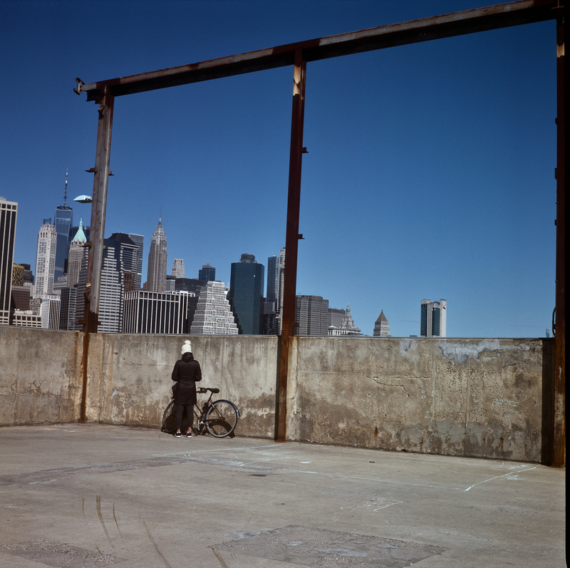 A picture of a lone person dressed for winter weather standing by a bicycle in Brooklyn Bridge Park in New York City. 