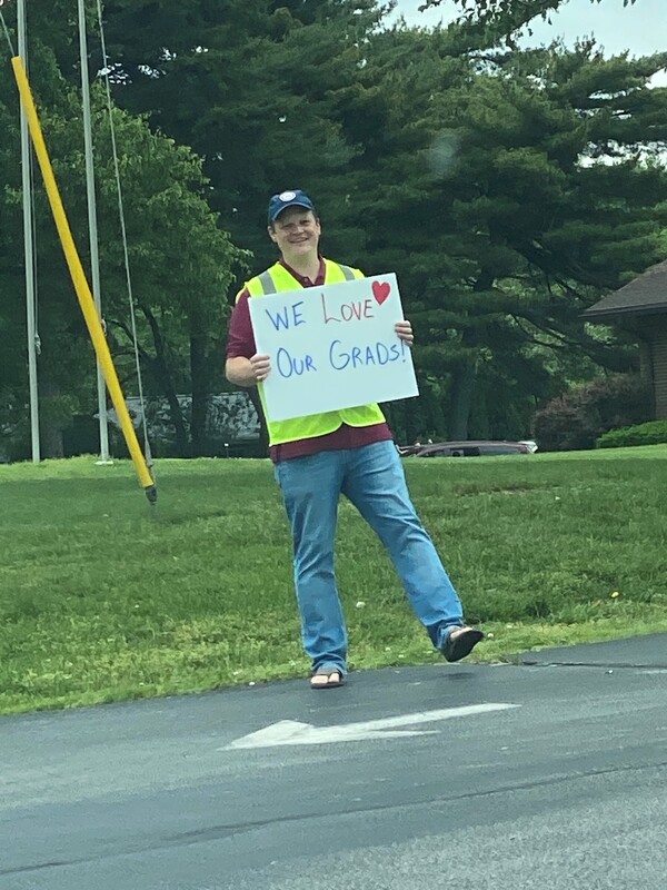A man holding a sign reading "We Love Our Grads".