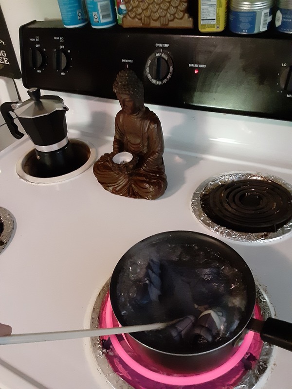 A person boiling face masks on a hot plate next to a buddha statue. 