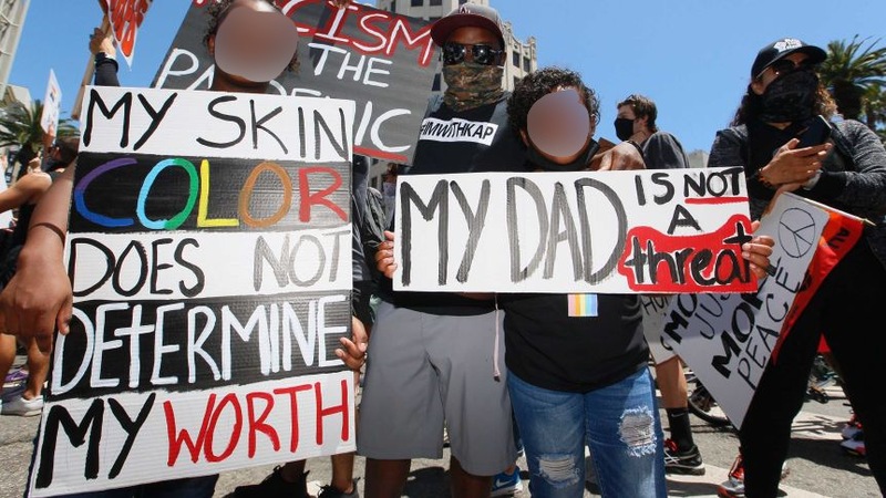 Image of protesters holding signs reading "My Dad Is Not a Threat" and "My Skin Color Does Not Determine My Worth". All the faces of protesters are blurred. 