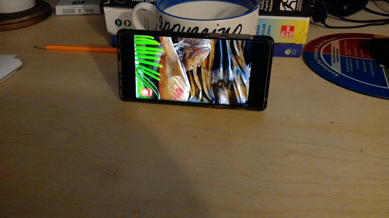 A phone playing a video laying against a mug.