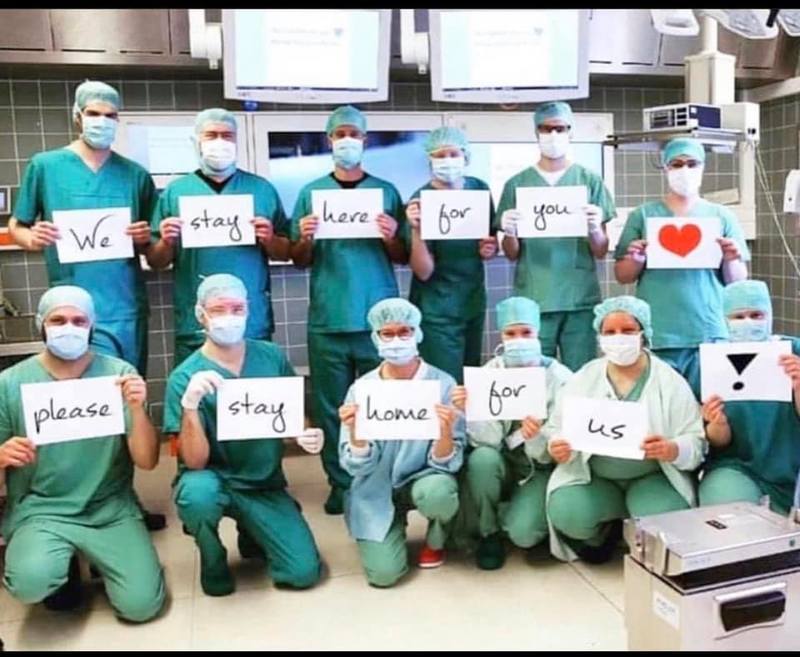 Image of doctors wearing masks holding signs that say we stay here for you please stay home for us.
