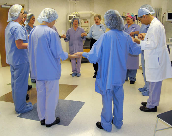 Healthcare workers are standing around in a circle holding hands. 