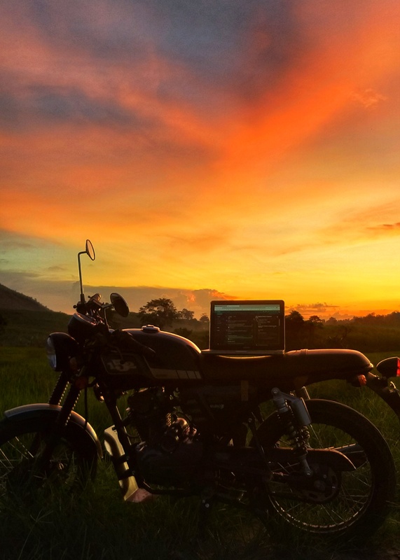 A motorcycle with a laptop on top of it photographed in front of a sunset.