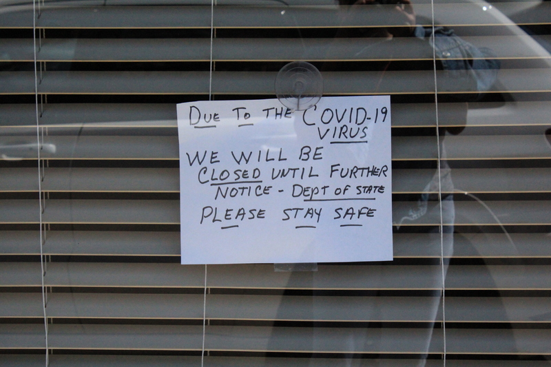 A business window with a hand written note in the window that says "Due to the COVID-19 virus we will be closed until further notice-Dept of State-Please stay safe."