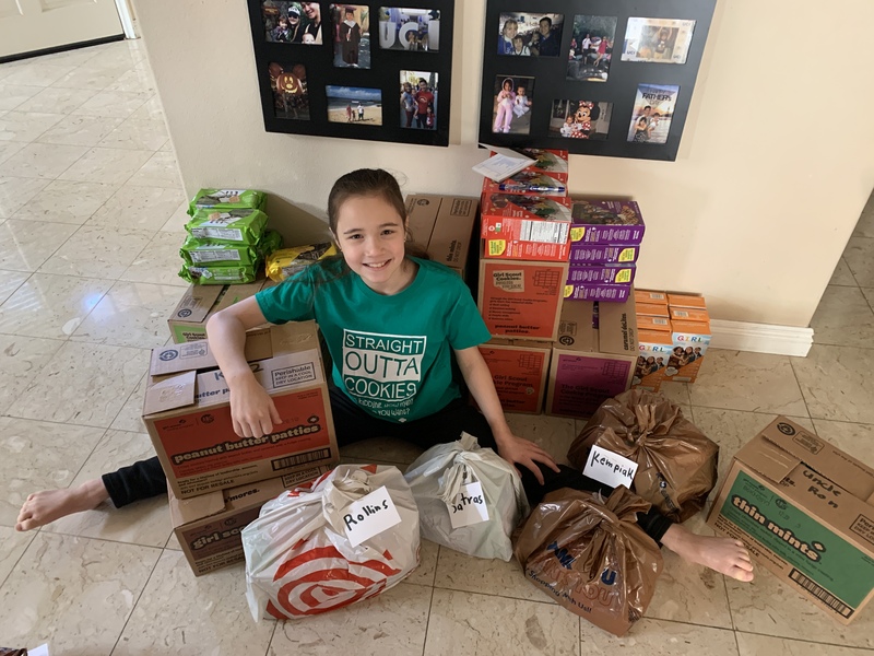 Young girl sits in front of boxes of Girl Scouts cookies on the floor.