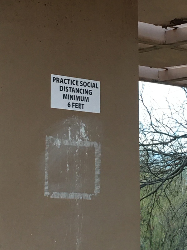 A sign that is on the side of a building telling people to practice social distancing. 