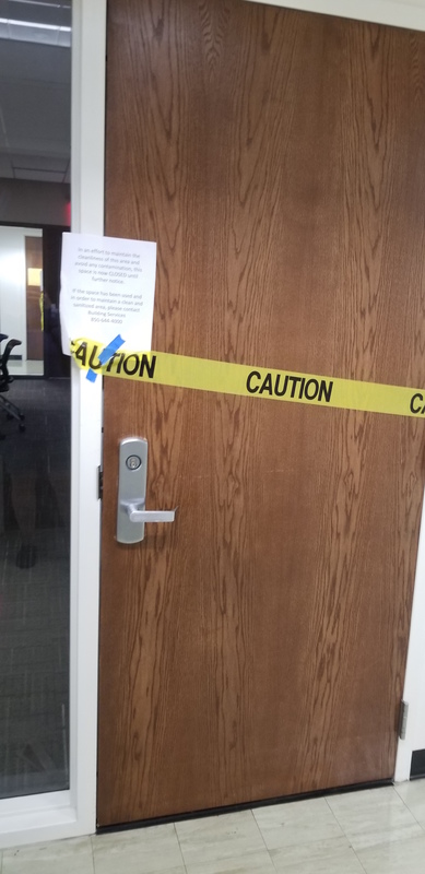 A wooden door with yellow caution tape blocking it off. There is also a piece of paper taped to the door frame. 
